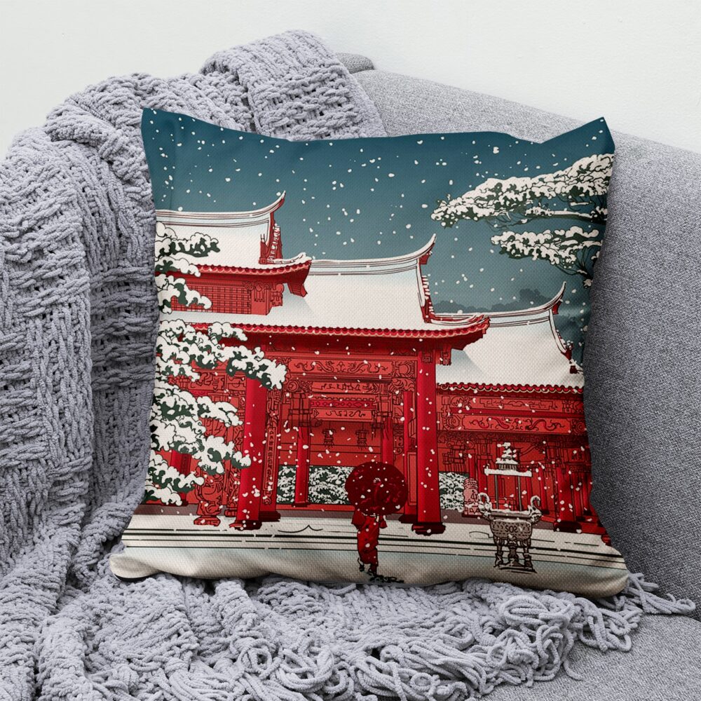 Coussin avec un bâtiment japonais rouge enneigé et un ciel bleu posé sur un canapé gris avec un plaid de la même couleur