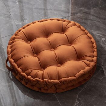Coussin rond et orange avec une poignée posé sur un sol gris.
