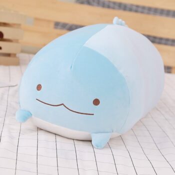 Coussin en forme de créature mignonne kawaii avec deux yeux et un sourire. Ce coussin est posé sur un tissu blanc à rayures noires.