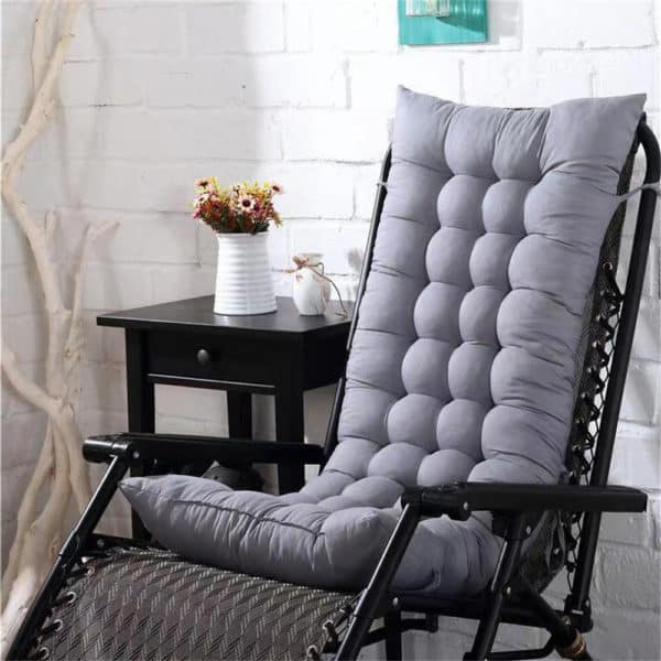 Coussin de chaise longue gris clair rembourré sur chaise longue noir. Table de chevet noire et pot avec fleurs en arrière plan.