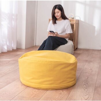 Pouf jaune tatami avec fille brune assise sur une chaise marron en arrière plan.