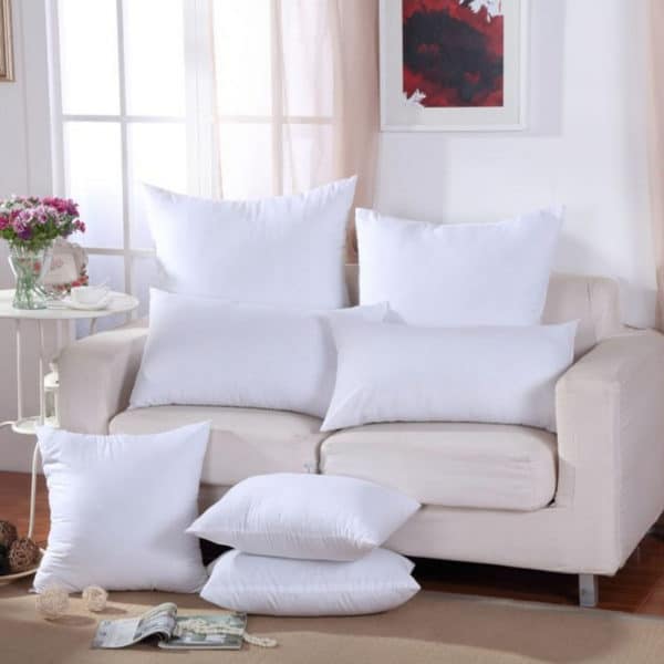 Plusieurs coussins blancs posés sur un canapé clair dans un salon.