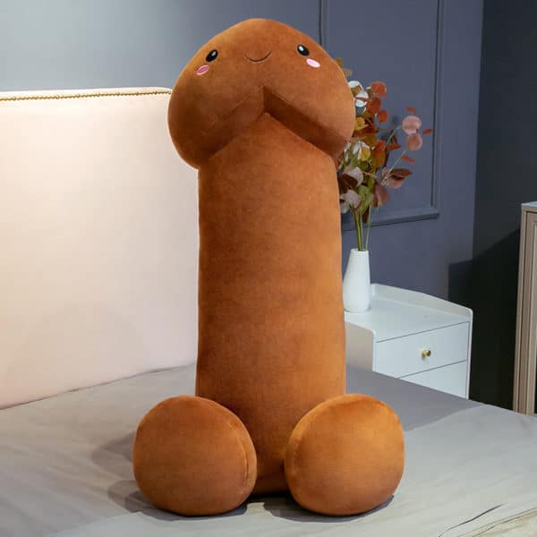 Coussin marron en forme de pénis posé sur un lit.