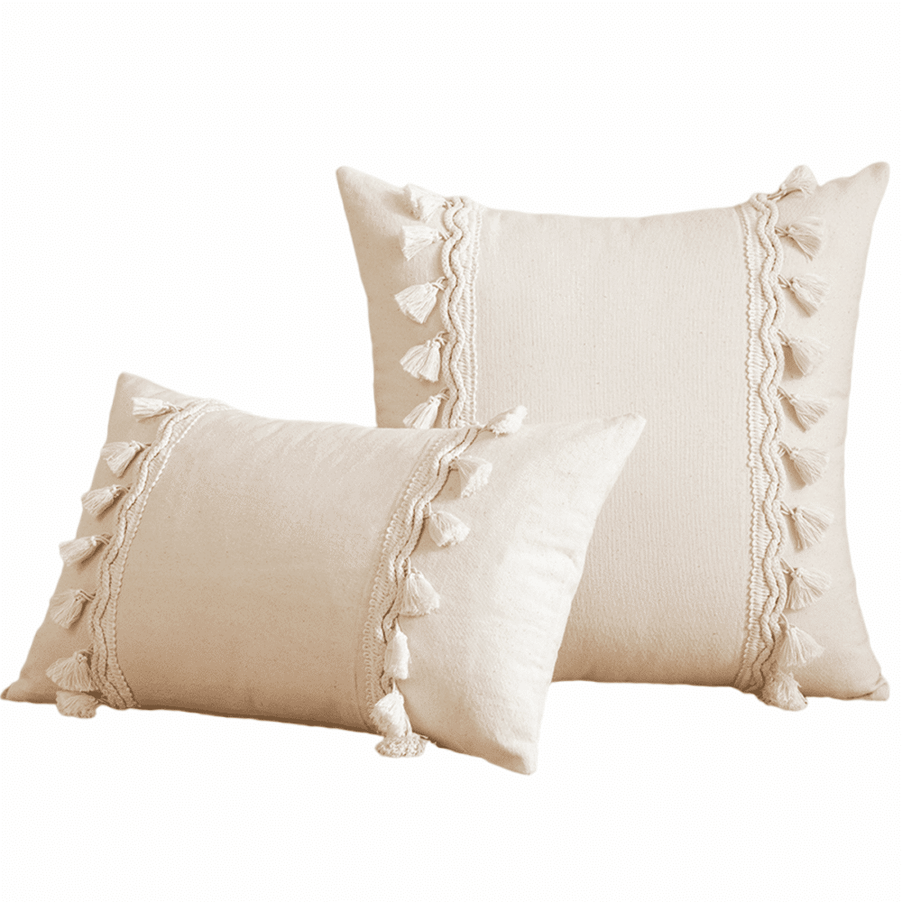 Deux coussins beiges posés l'un contre l'autre. Premier coussin rectangulaire et deuxième carré, les deux avec des pompons en macramé