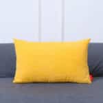 Coussin rectangulaire jaune sur un canapé gris.