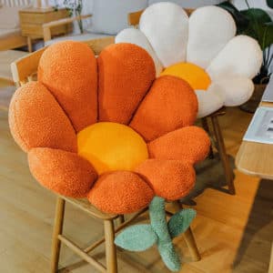 Coussins en forme de fleur orange et blanc posés sur des chaises en bois dans une pièce avec du parquet au sol.