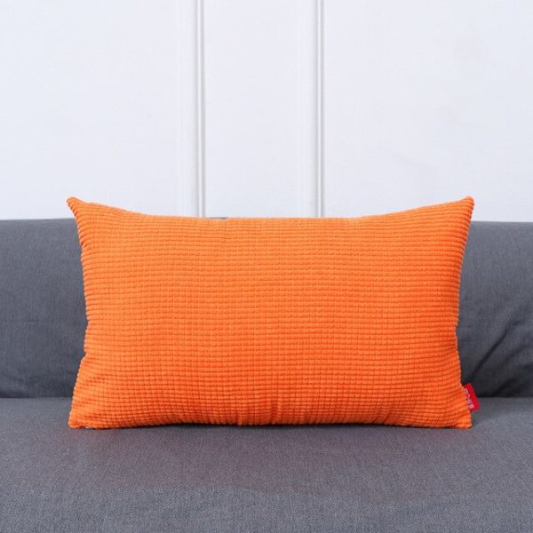 Coussin rectangulaire orange posé sur un canapé gris foncé.