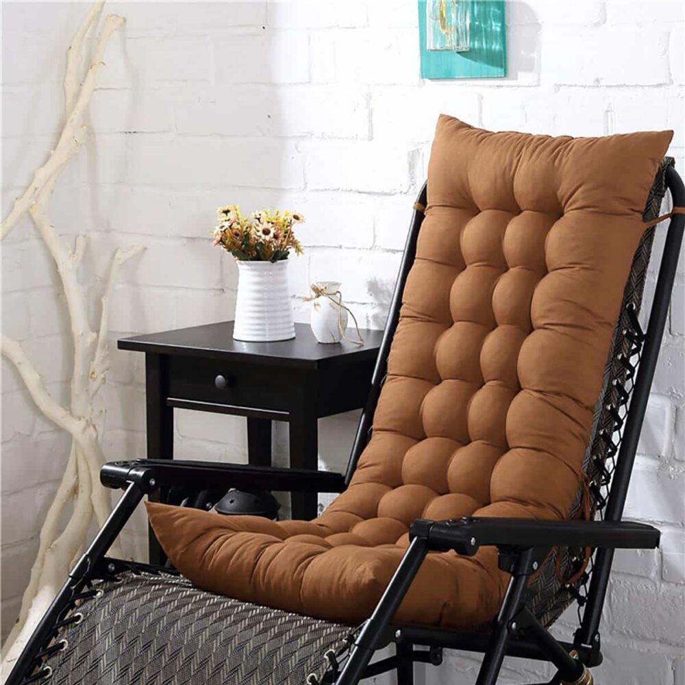 Coussin rectangulaire long marron posé sur un transat noir, table avec vase dans le fond de limage