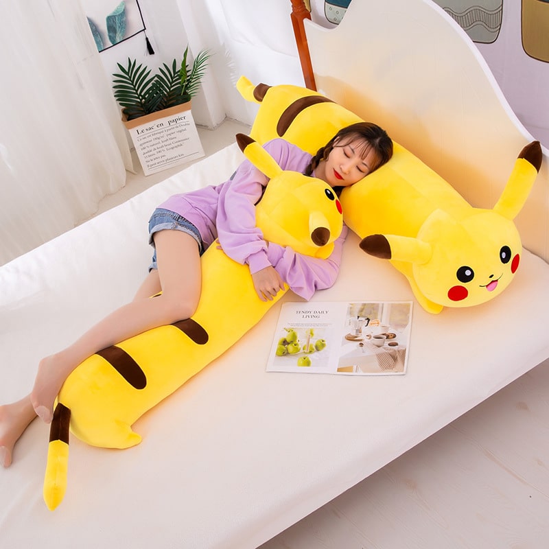 Femme couchée sur un lit, la tête sur un coussin Pikachu jaune, forme cylindrique et long, elle est également, le corps blotti sur un autre coussin pikachu