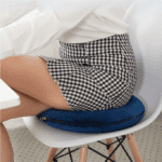 Femme assise sur un coussin circulaire pour soin du coccyx. Le coussin est lui même sur une chaise de couleur blanche
