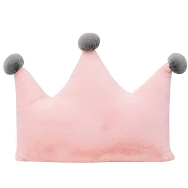 Joli coussin en forme de couronne. Ilest rose avec des pompons gris au sommet de chaque pointe de la couronne.