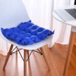 Coussin gonflable bleu posé sur une chaise blanche avec des pieds en bois. Parquet en bois et bureau banc avec un ordinateur portable posé dessus.