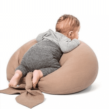 Coussin de grossesse beige taupe en forme de U, les extremités représentent une feuille. Il y a un bébé d'environ 8 mois à l'intérieur, de dos.