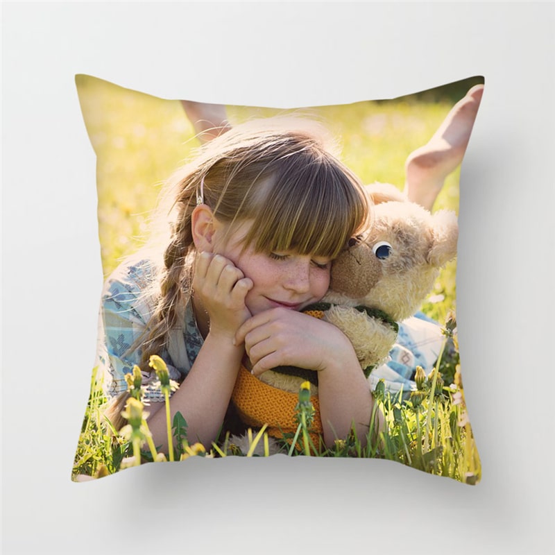 Housse de coussin imprimé d'une photo de petite fille couchée sur le ventre dans l'herbe et tenant dans sa main gauche une peluche
