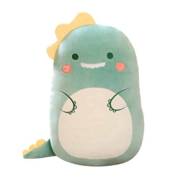 Coussin dinosaure vert clair kawaii souriant avec des dents blanches, un cœur rose sur chaque joue, un cercle blanc en guise de ventre et deux mains dessinée, le dinosaure a une crête jaune sur la tête et une petite queue avec une crête jaune à l'extrémité.