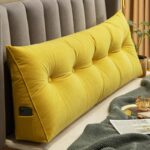 Coussin tête de lit jaune en position debout présent dans une chambre et positionné sur un lit. Le coussin tête de lit jaune a une poche sur la gauche, à lintérieur de cette poche il y a un téléphone portable.
