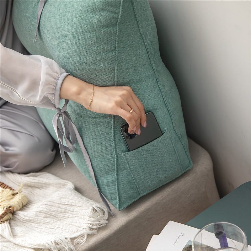 Coussin tête de lit vert en position debout sur un lit, le lit est situé dans une chambre. Une main féminine prends le téléphone portable présent dans la poche gauche du smartphone.