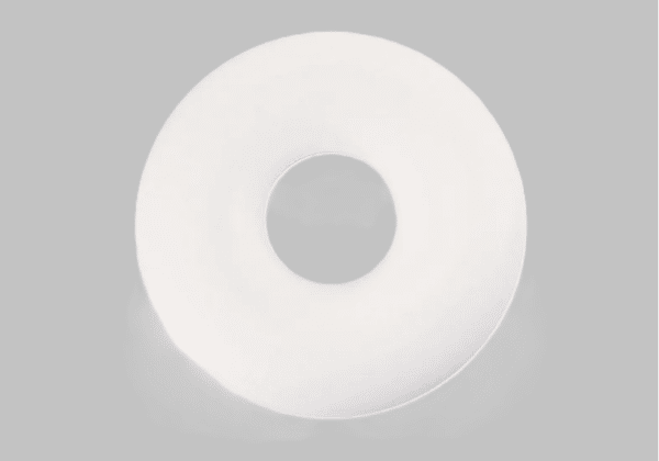 coussin circulaire en forme de donut de couleur blanche sans la couverture. Le coussin est derrnière un fond gris