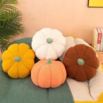 Quatre coussins en peluche de potiron orange, blanc, jaune et marron sont posés sur un canapé