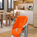 Coussin de chaise en cuir (Peg Perego Prima Pappa Zero3) de couleur orange posé sur une chaise haute grise, la chaise est dans une cuisine.