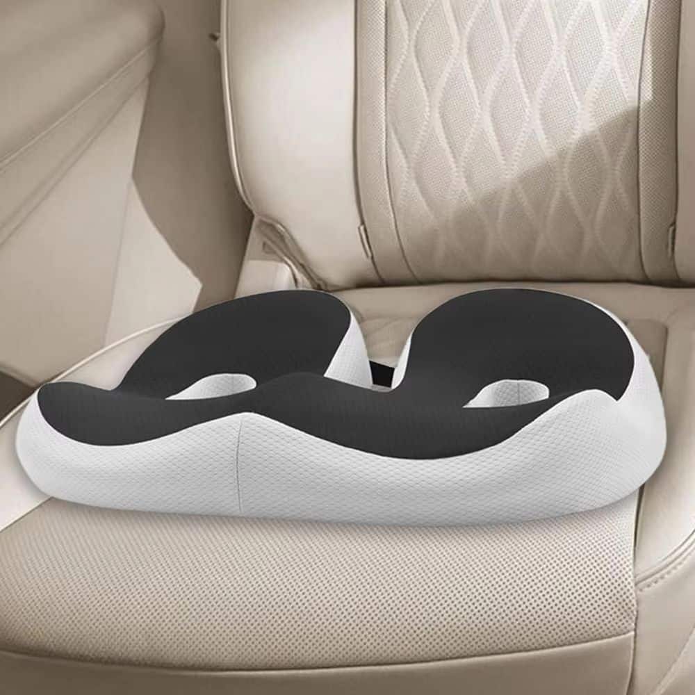 Coussin de siège ergonomique de couleur noir en forme de U avec deux trous d'aération et une bande élastique équipée d'une fermeture à boucle pour adapter la taille du coussin à vos fesses. Le coussin est posé sur un siège de voiture de couleur beige.