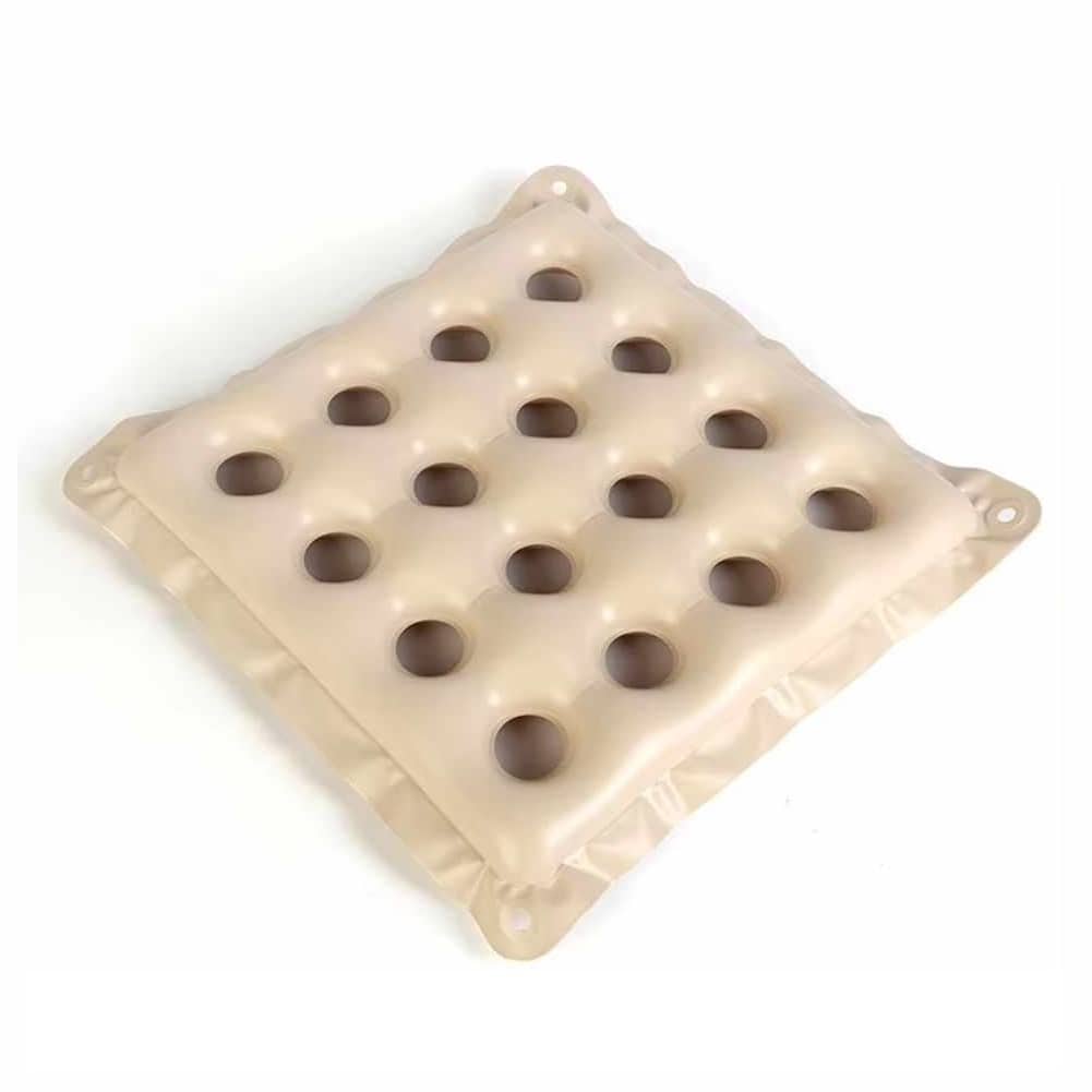 Coussin gonflable anti-escarre de couleur beige, conçu avec une structure en grille comprenant 16 trous circulaires. Le coussin est muni de quatre œillets aux coins pour le fixer en place. Le coussin est posé à même le sol.