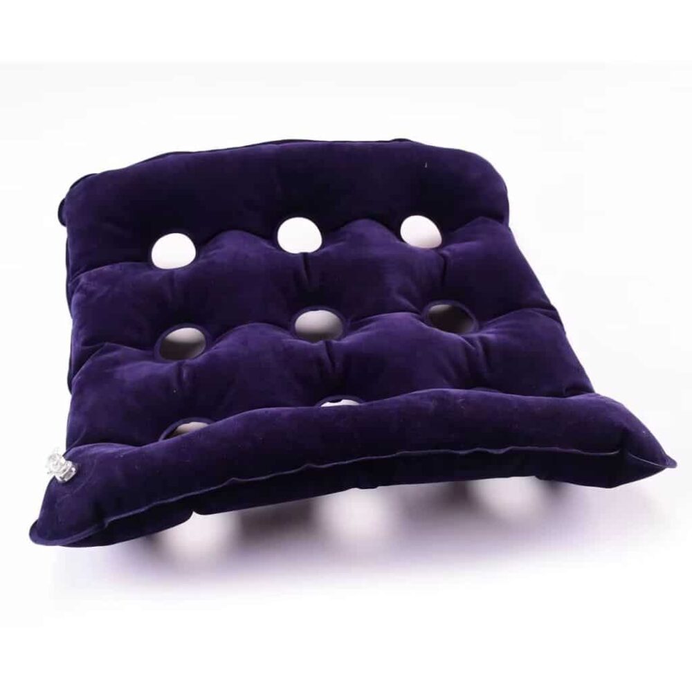 Coussin gonflable anti-escarre de couleur violet foncé, fabriqué dans un matériau au toucher velours. Il possède 9 trous circulaires répartis de manière uniforme. Une valve transparente est visible sur le côté, permettant de gonfler ou de dégonfler le coussin.