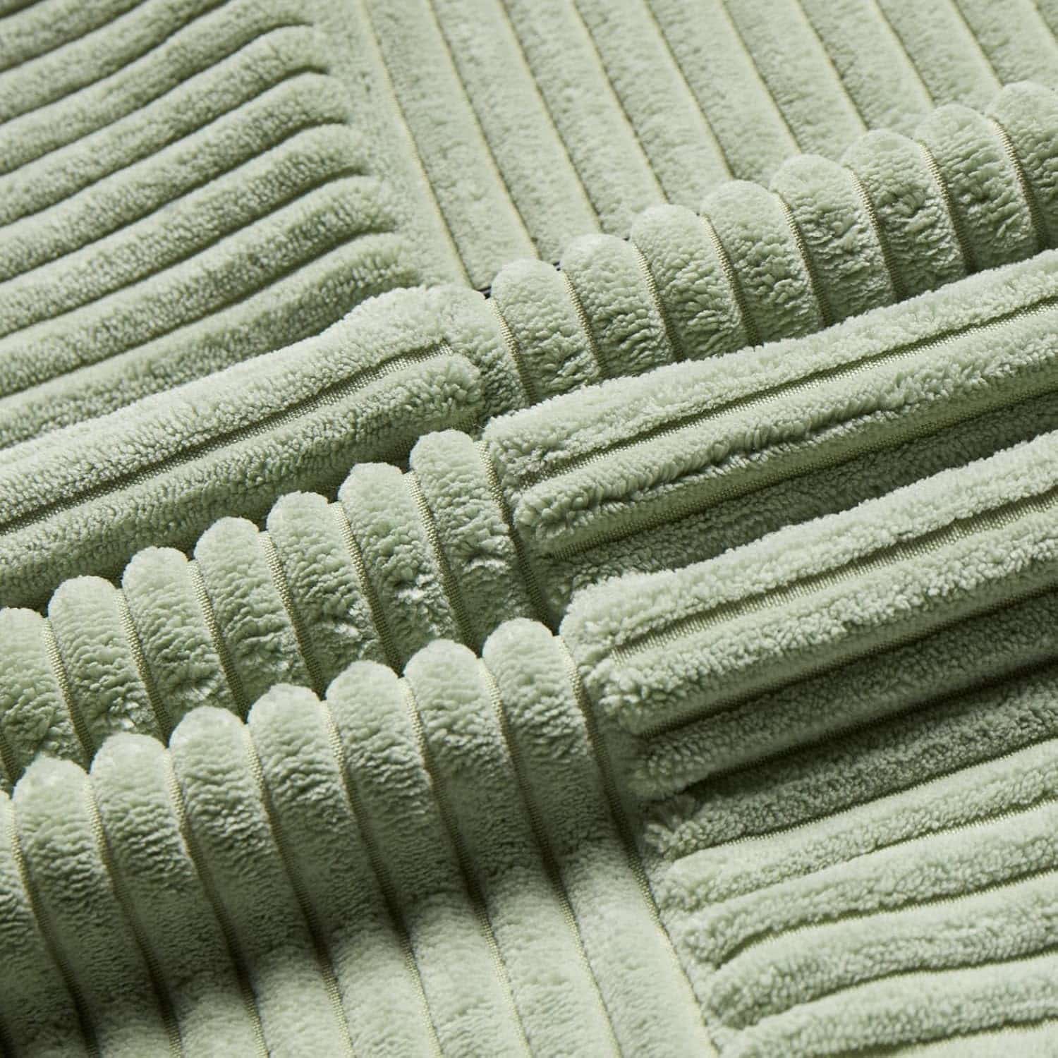 gros plan très détaillé du tissu d’un coussin en velours côtelé vert sauge avec ses bandes orientées dans différentes directions (verticale, horizontale, diagonale), créant un effet patchwork géométrique.